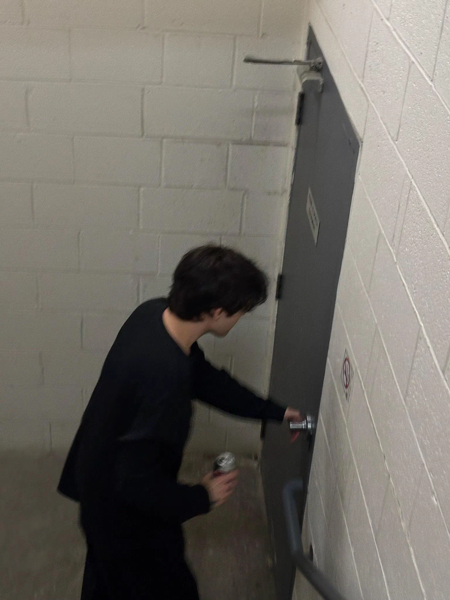 Andrada opening a stairwell door, a can in one hand.