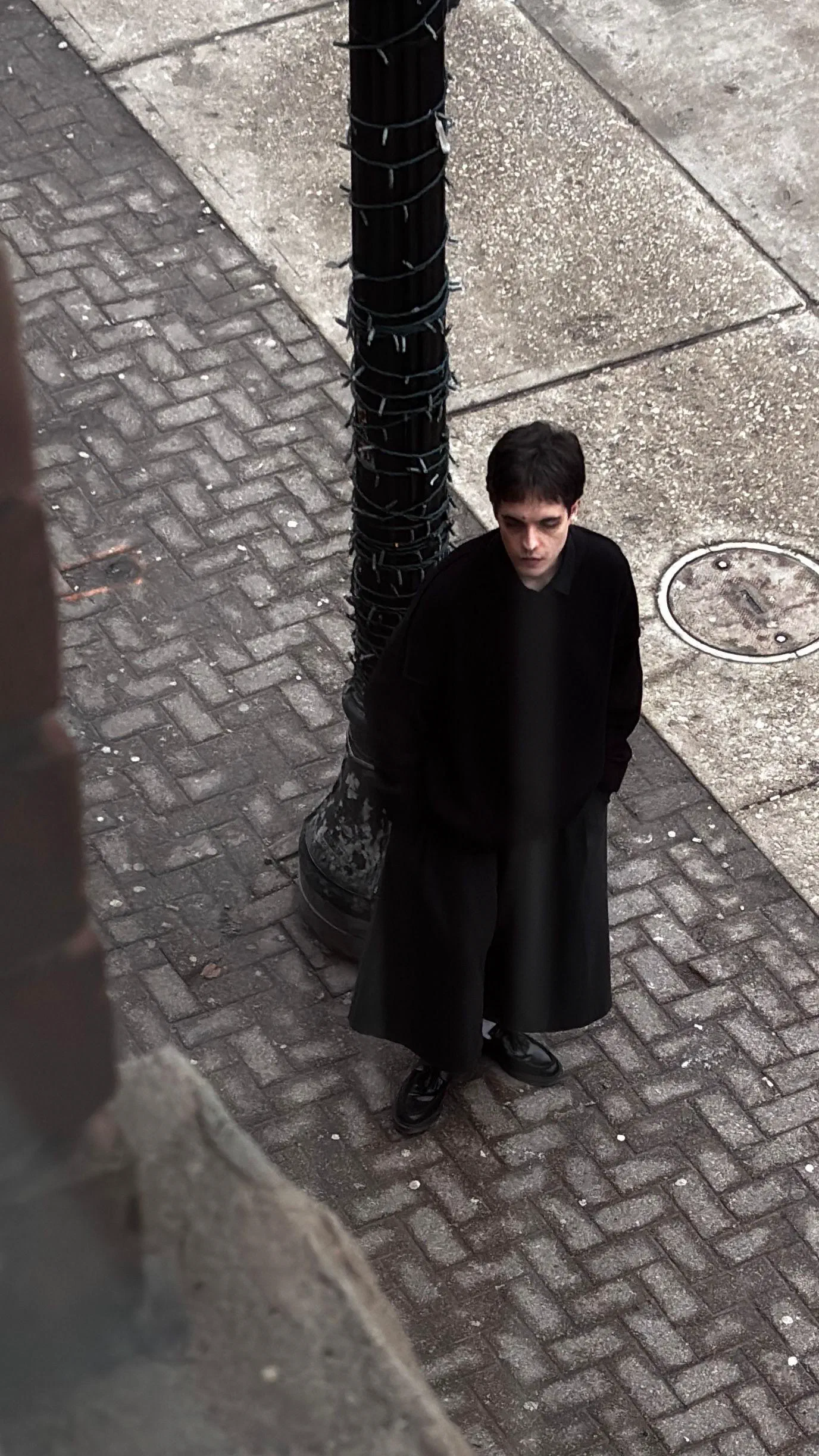 Andrada at the same lamppost, hands in his pockets, photographed from above, March 2026.