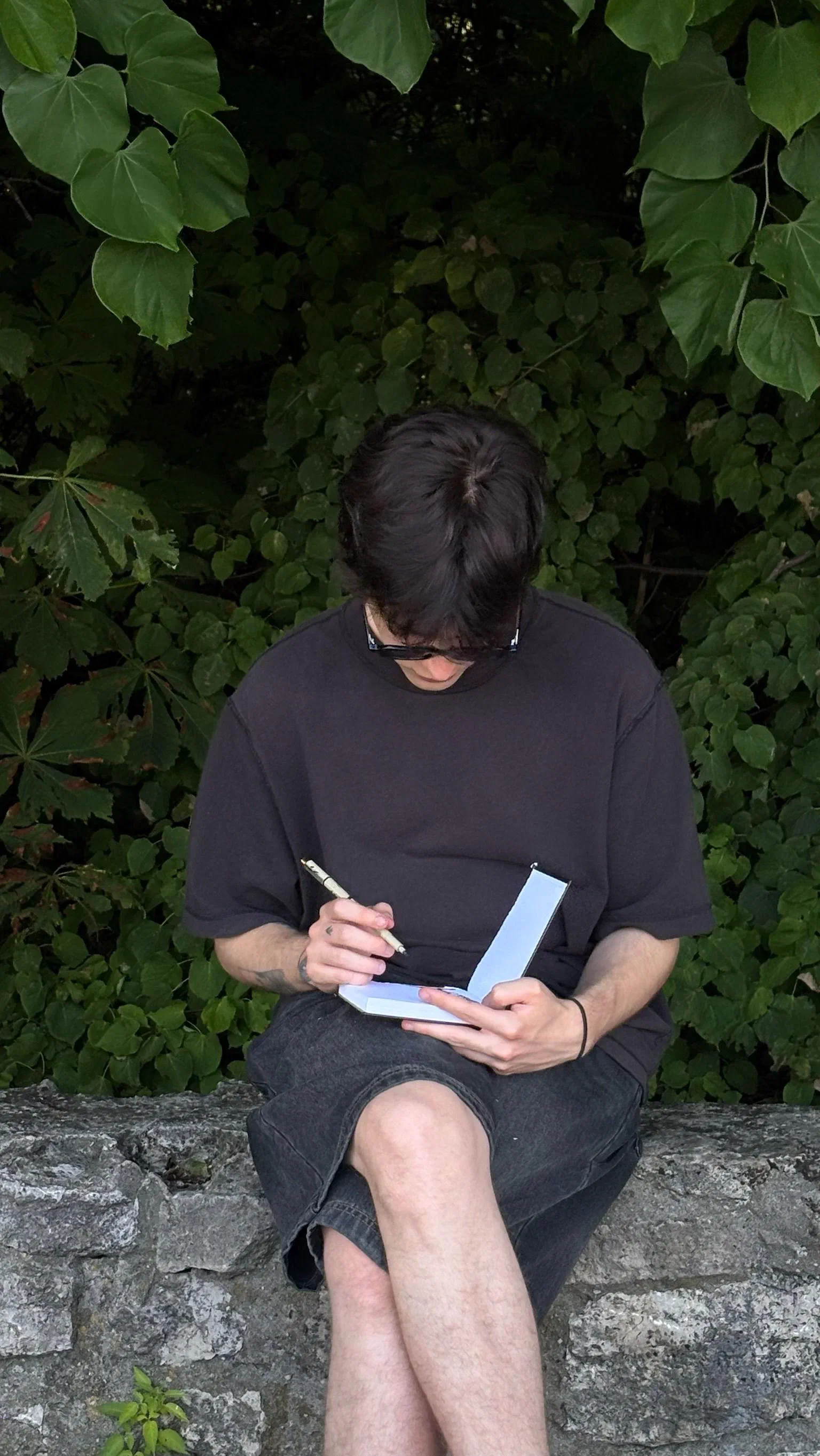 Andrada sketching in a pocket notebook on a stone wall, August 2026.