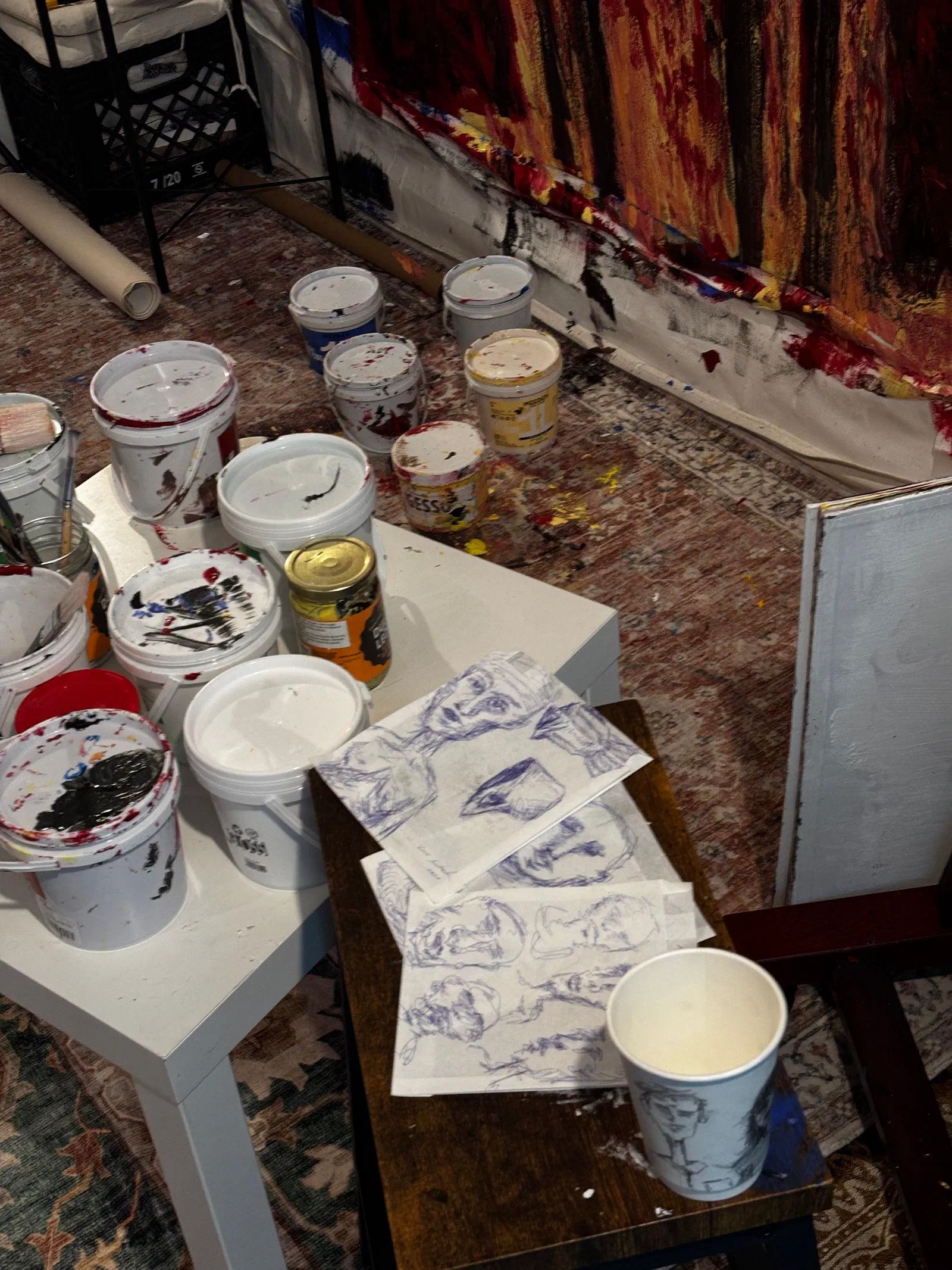 Paint tubs and ballpoint sketches of faces on a studio table, July 2026.